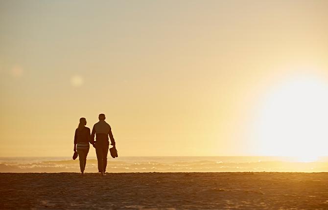 Two people walk hand in hand on the beach at sunset.