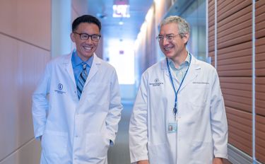 Two MSK physician-scientists wearing white lab coats smile while walking side by side. 