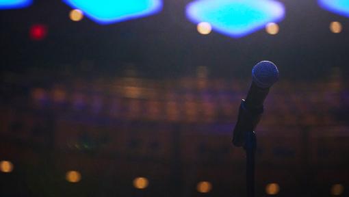 Closeup image of a microphone on a stand with stage lights behind it.