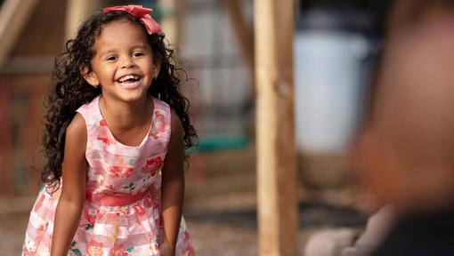 A young girl in a pink dress stands and laughs.