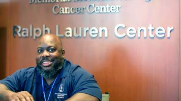 A man smiles at the camera from in front of a Ralph Lauren Center sign. 